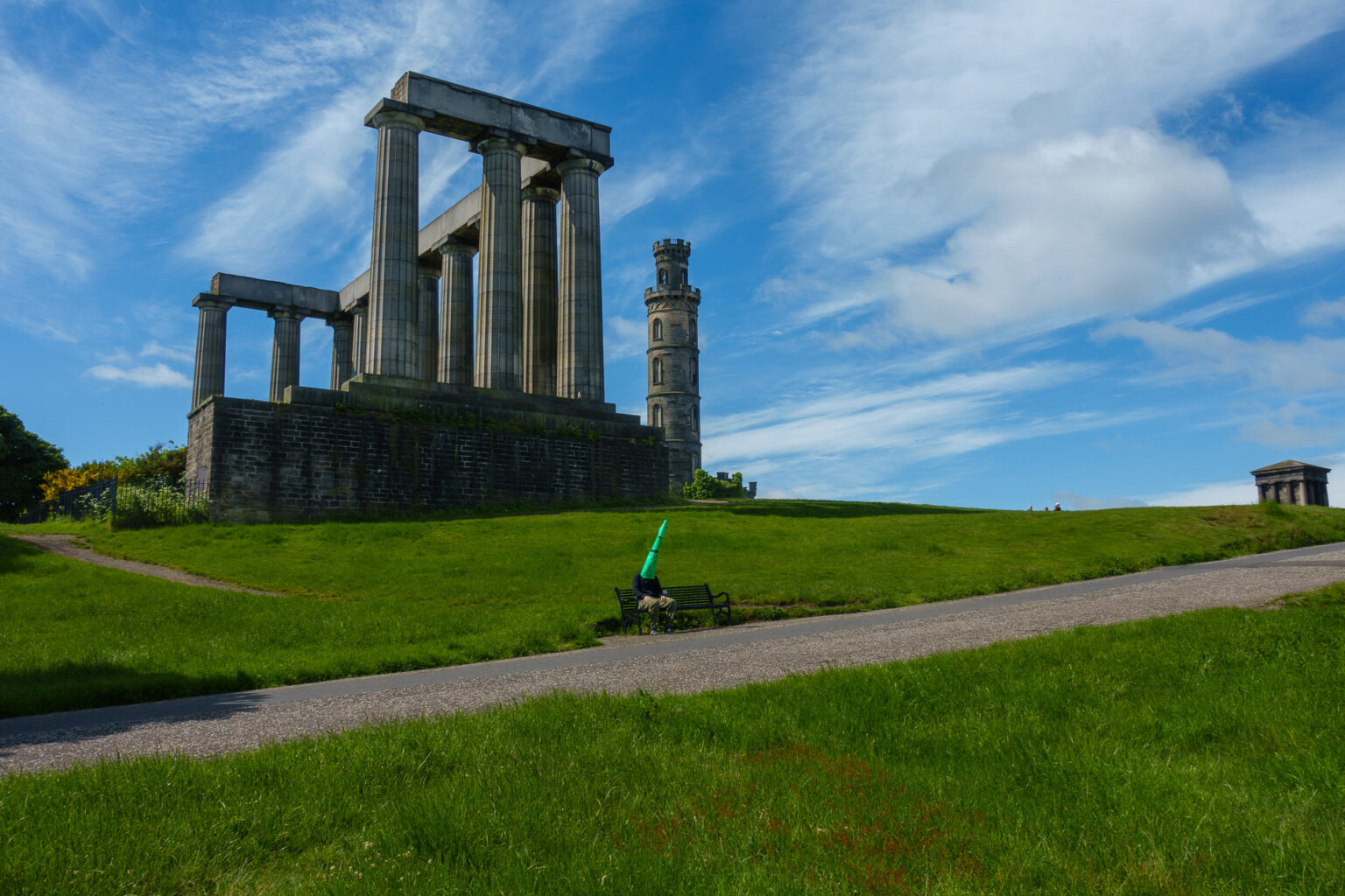 Wojtek sitting on a bench, with Calton Hill half-Partenon behind his back