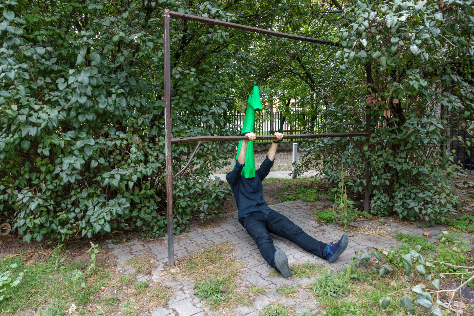 Wojtek dressed as a green monster does flip-ups on a metal rack in a Polish, derelict garden