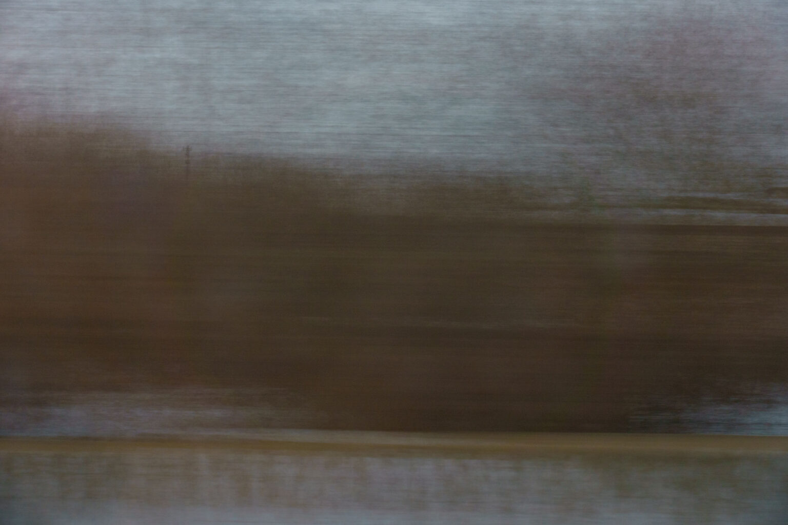 A blurry landscape image shot through a window on a moving train