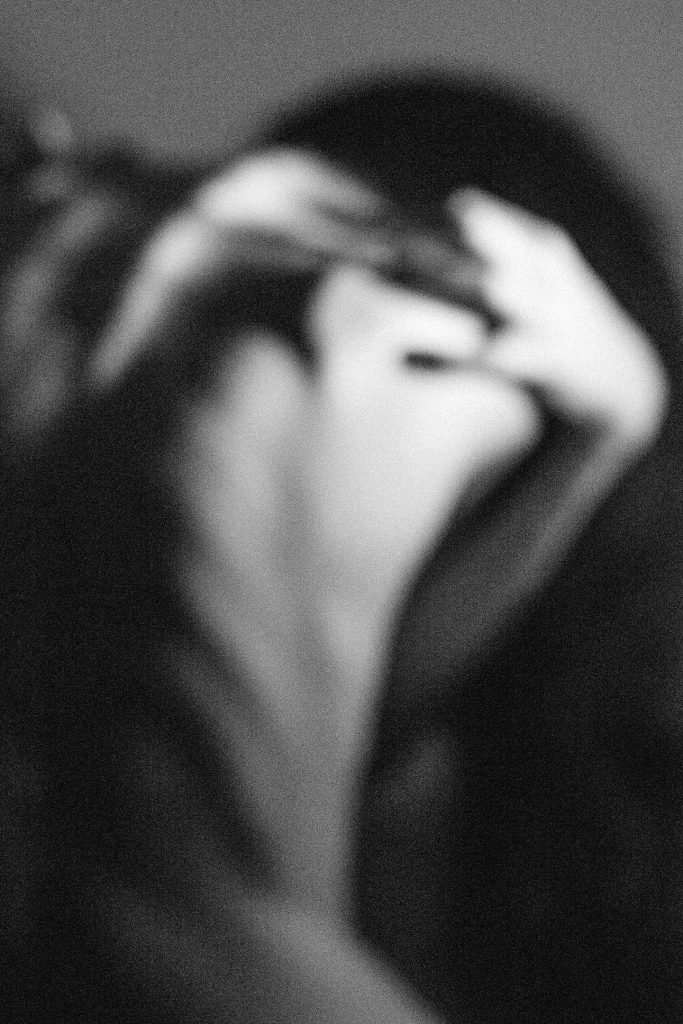 Photograph of a woman's back, desperately holding her hands behind her neck, with bones visible under the skin.