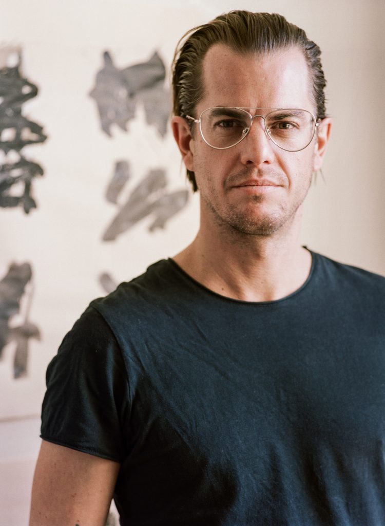 Portrait of Jonathan Freemantle with one of his paintings in the background.