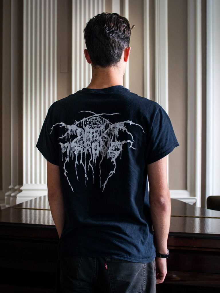 Male model standing with their back to the camera, wearing a tshirt with a black metal band's logo