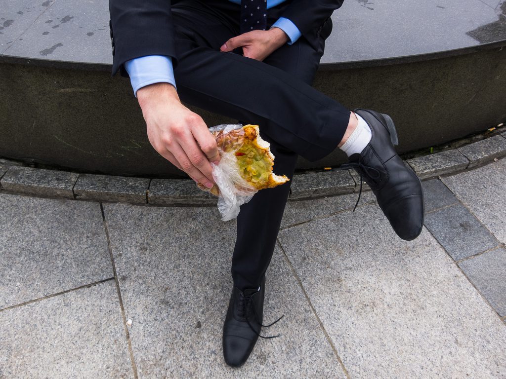 Photograph of a blue-collar worker eating a rough-looking sandwich.