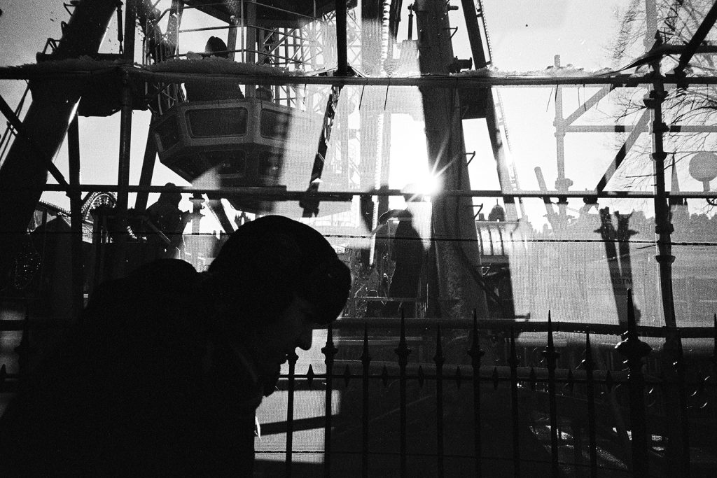 A winter photograph of a man sadly walking with a silhouette of a Ferris wheel in the background